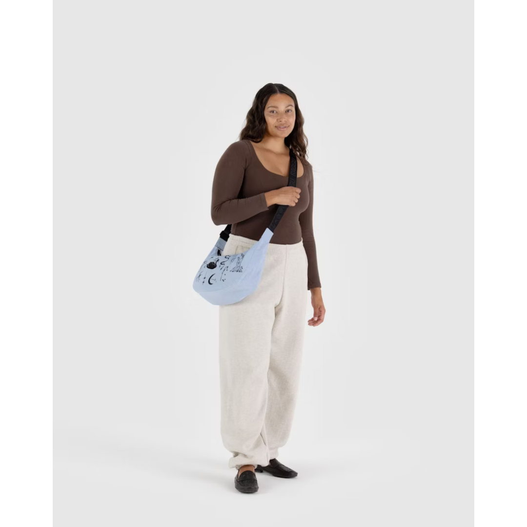 Woman carrying a baby blue nylon bag featuring black embroidery of a bow, a swan, a snake, a moon, a hand, a spider, stars and a rose. Also features a black strap.
