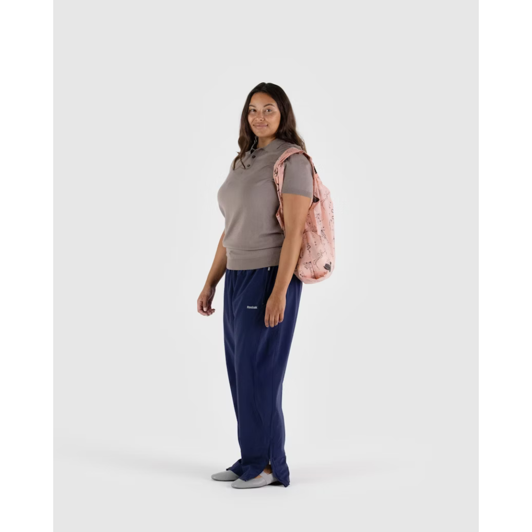 Woman carrying baby pink reusable tote bag featuring a black pattern of swans, moons and stars, bows and ballet slippers.