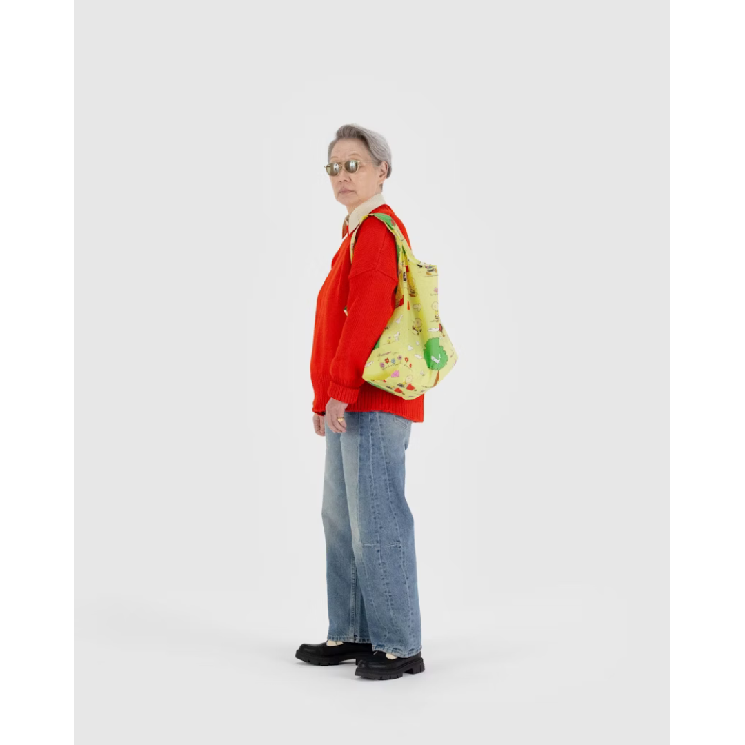 Woman holding yellowish green reusable tote bag featuring a Charlie Brown and Snoopy print flying kites into trees.