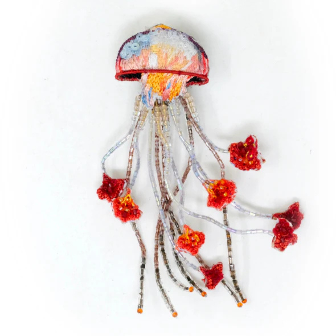 Hand embroidered and beaded jellyfish brooch magically floats along. the top of the jellyfish is colored in blues, pink, peach, yellow, orange and red and covered in clear micro sequins. The tentacles are made of clear and bronze beads and have red beaded, flowerlike, bulbs at the end.