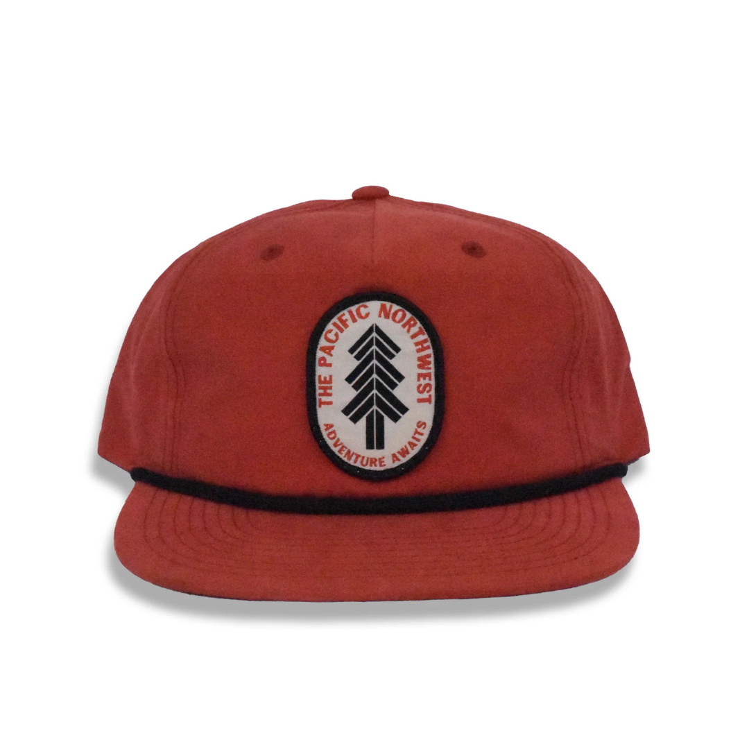 Soft orange 5 panel cap in dark orange with black trim featuring an oval white patch with a black spruce tree graphic around the tree it says "The Pacific Northwest/Adventure Awaits" in orange.