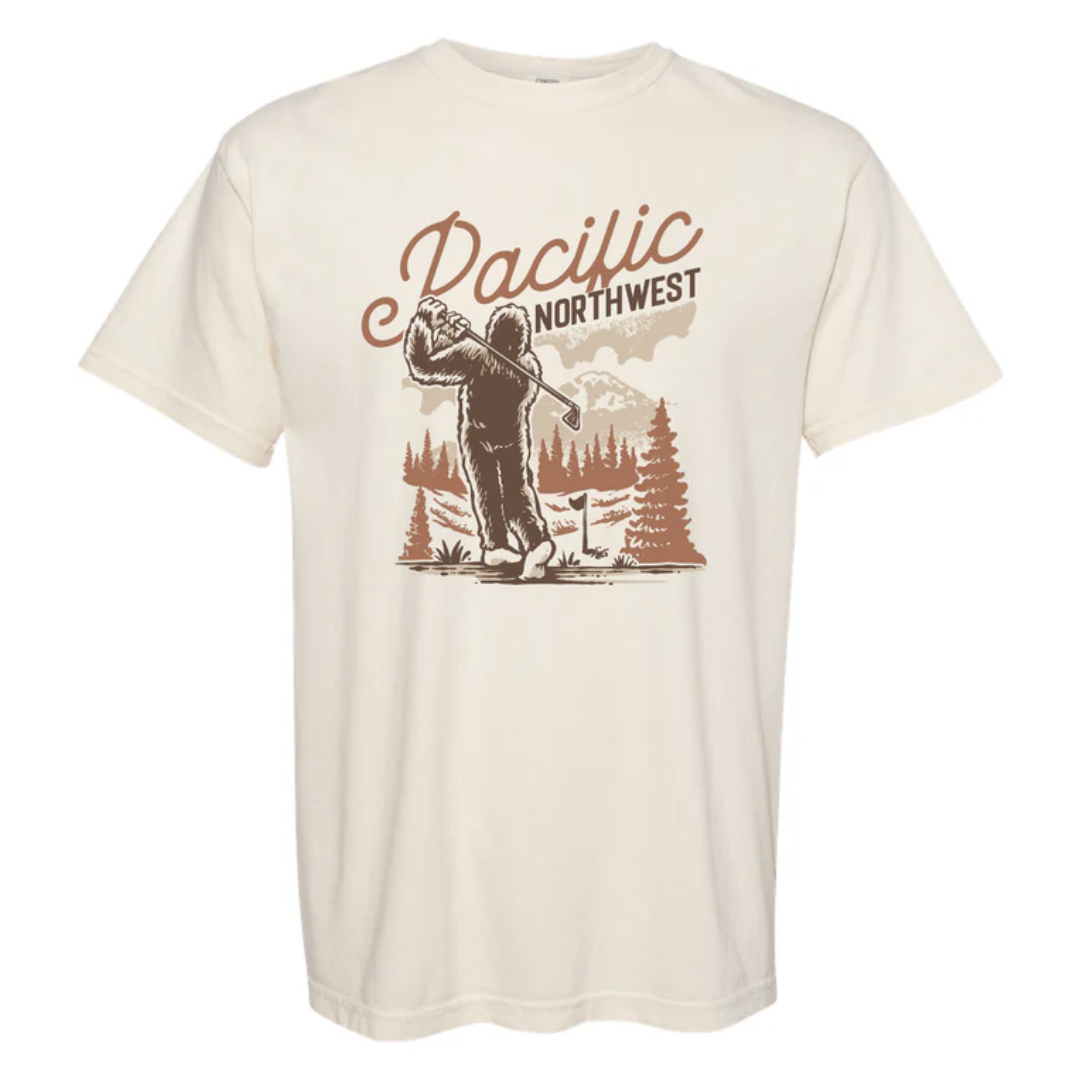 Ivory shirt with Sasquatch golfing among the pine trees reads "Pacific Northwest"