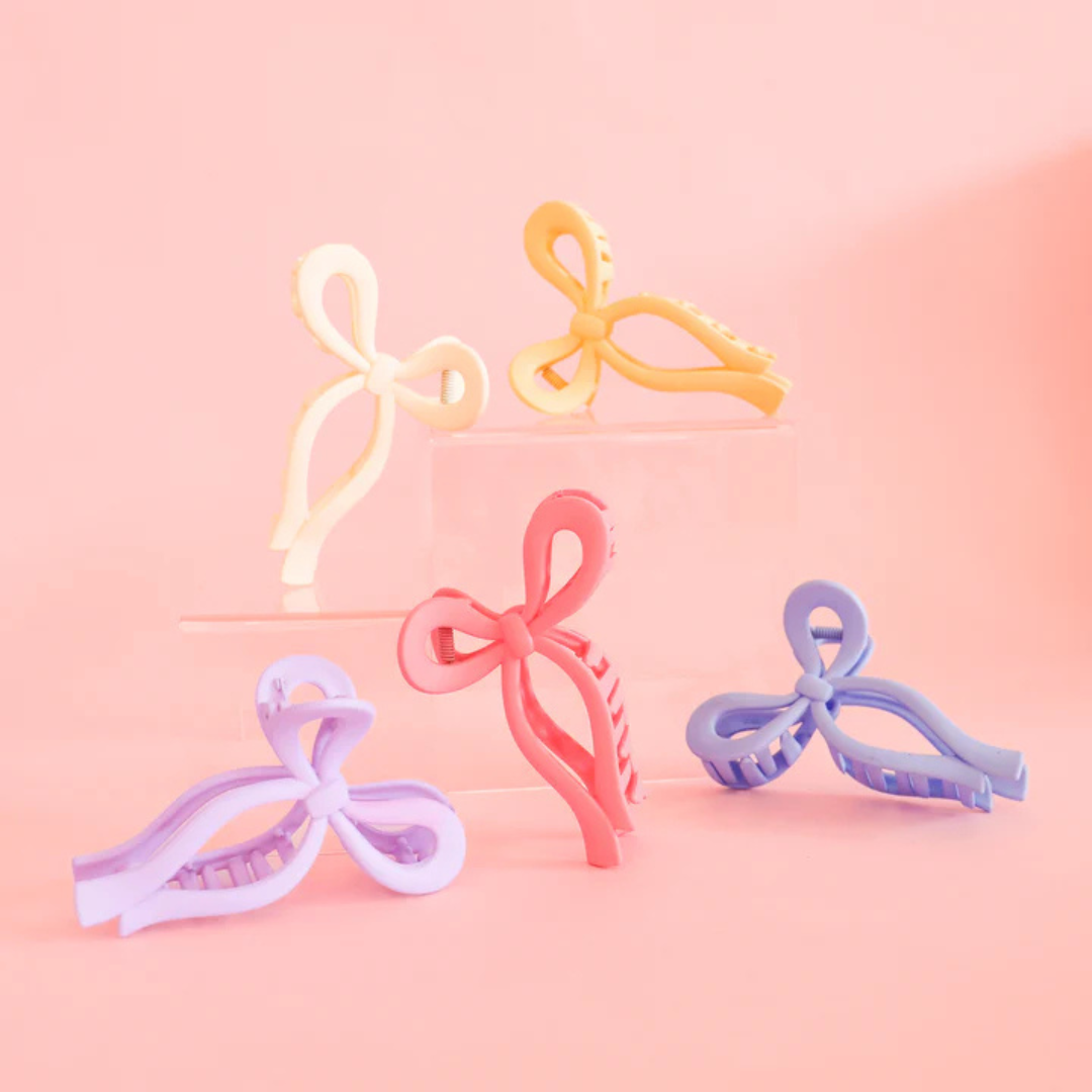 Collection of cream, yellow, lilac, pink, and periwinkle bow clips against a pink background