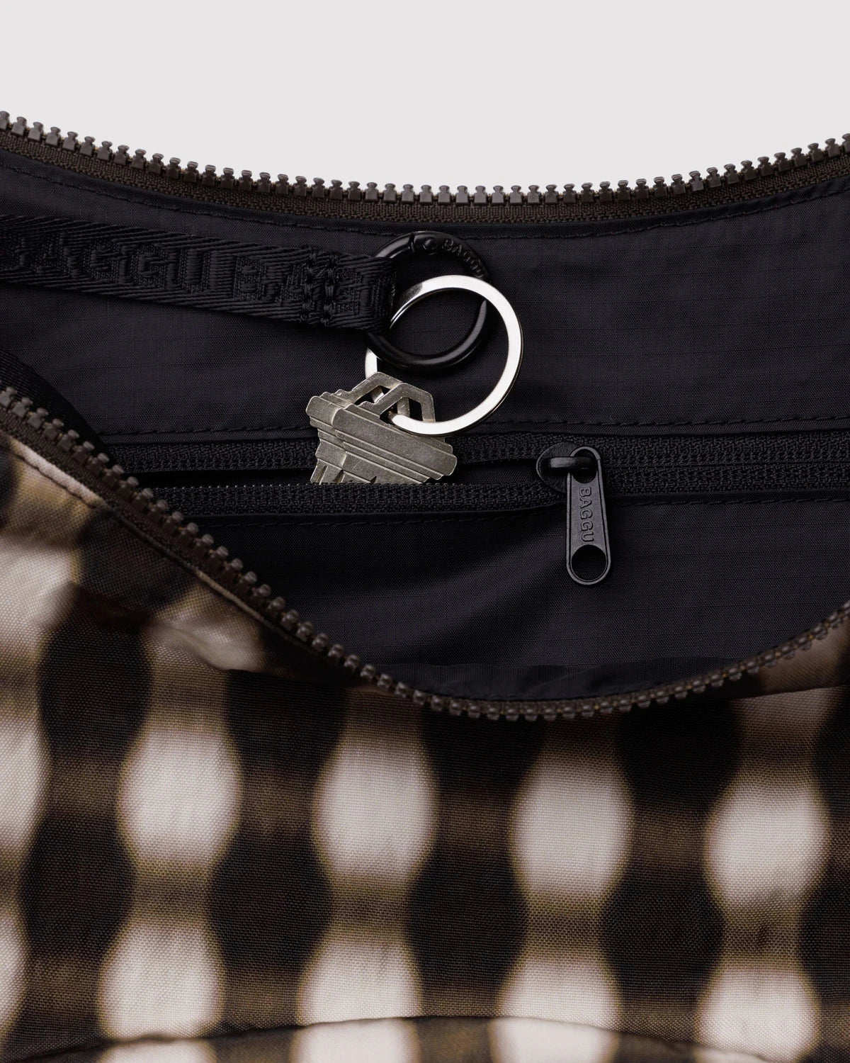 Close-up of a black bag with a zipper and a keychain on a checkered background