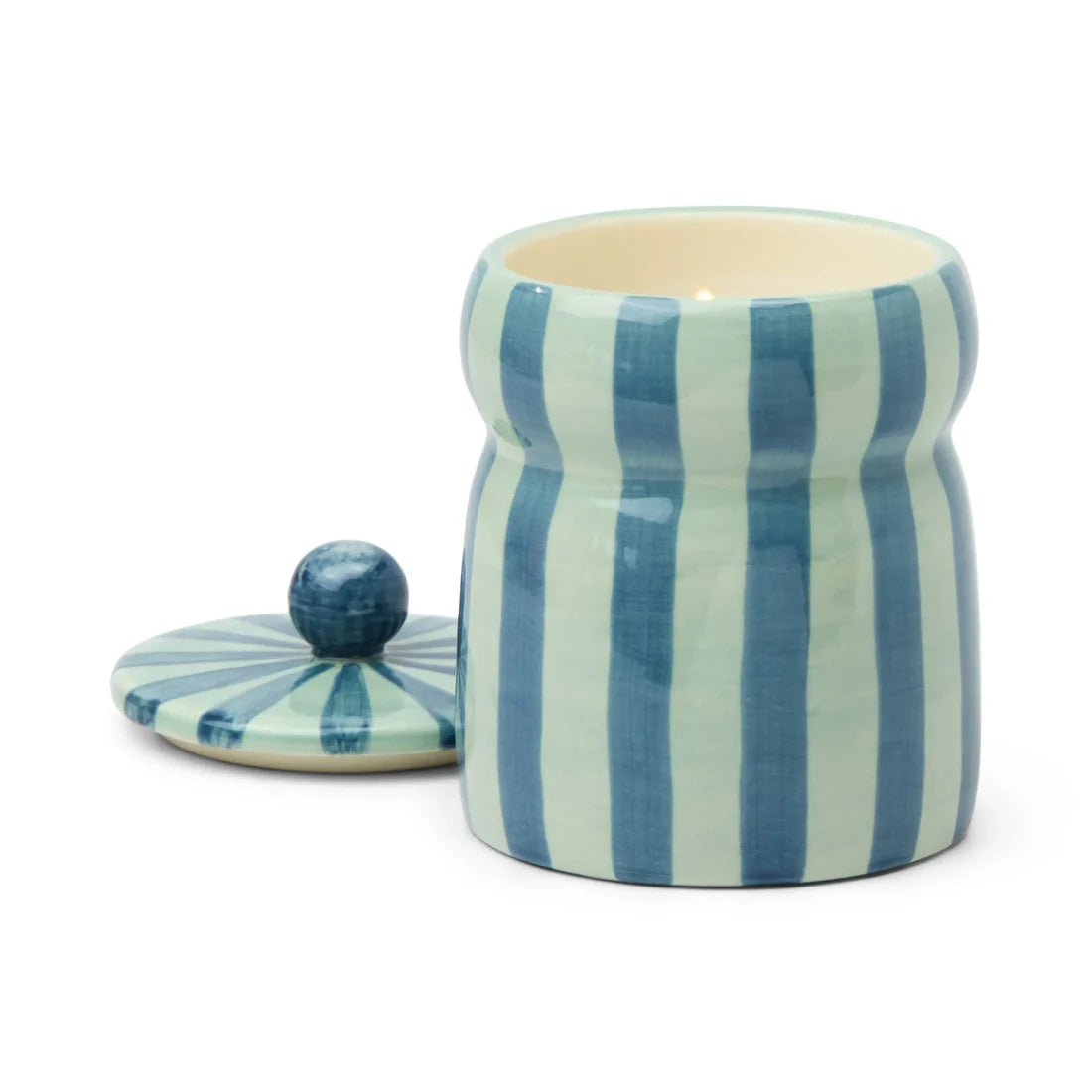 Candle with the lid removed and the candle lit inside the light blue and navy striped vessel.