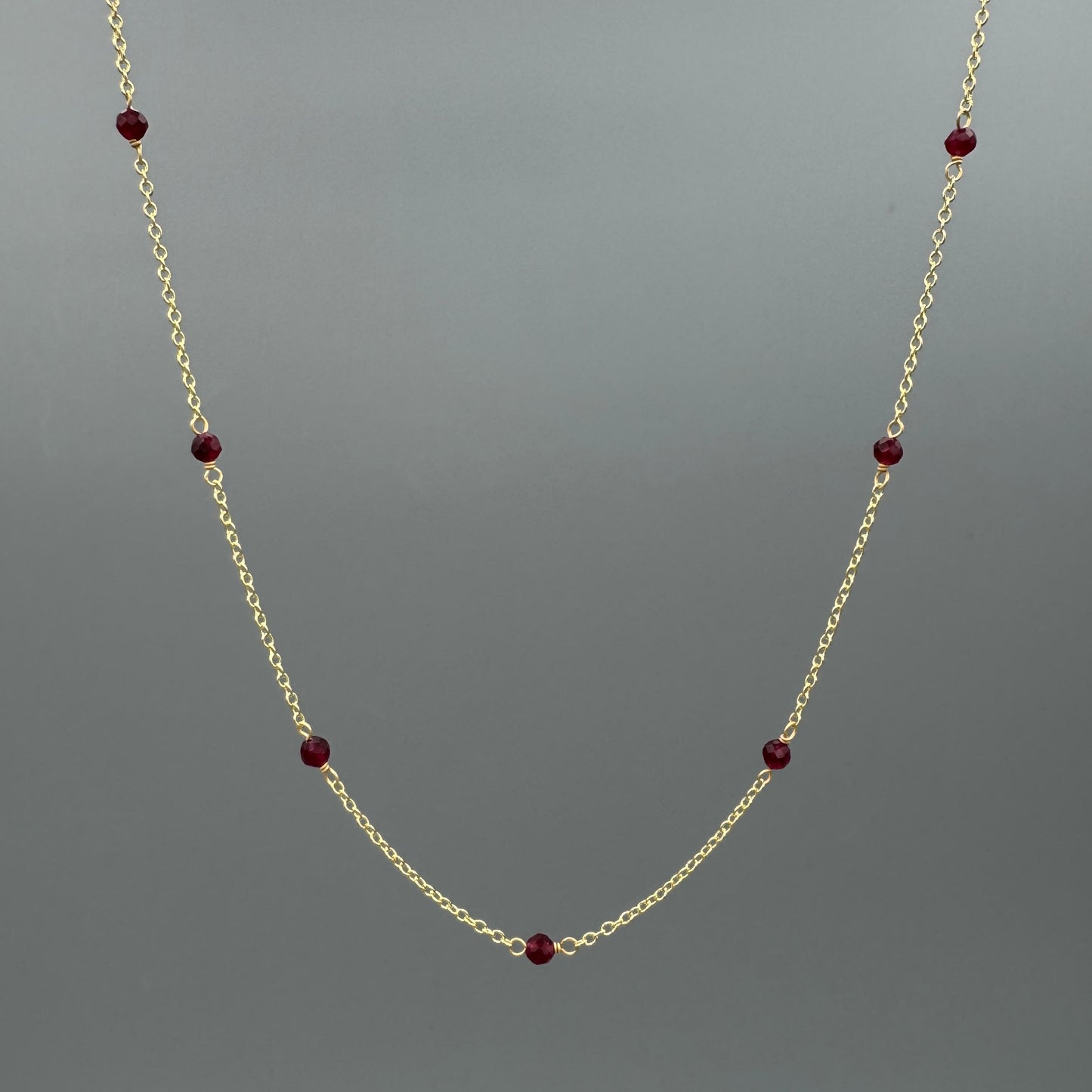 Gold necklace with dyed red beads on a gray background