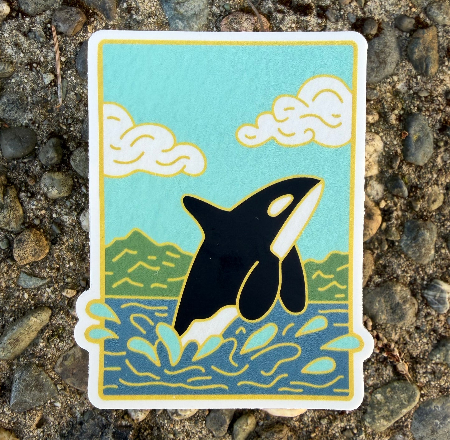 Sticker design featuring an orca jumping out of the water with mountains behind on a rocky background.