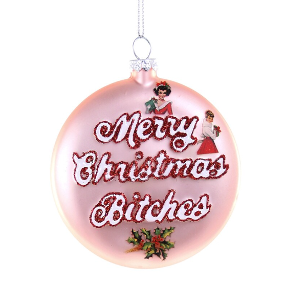 Pink ornament says "Merry Christmas Bitches" in glitter with decals of holly and vintage ladies in holiday finery.
