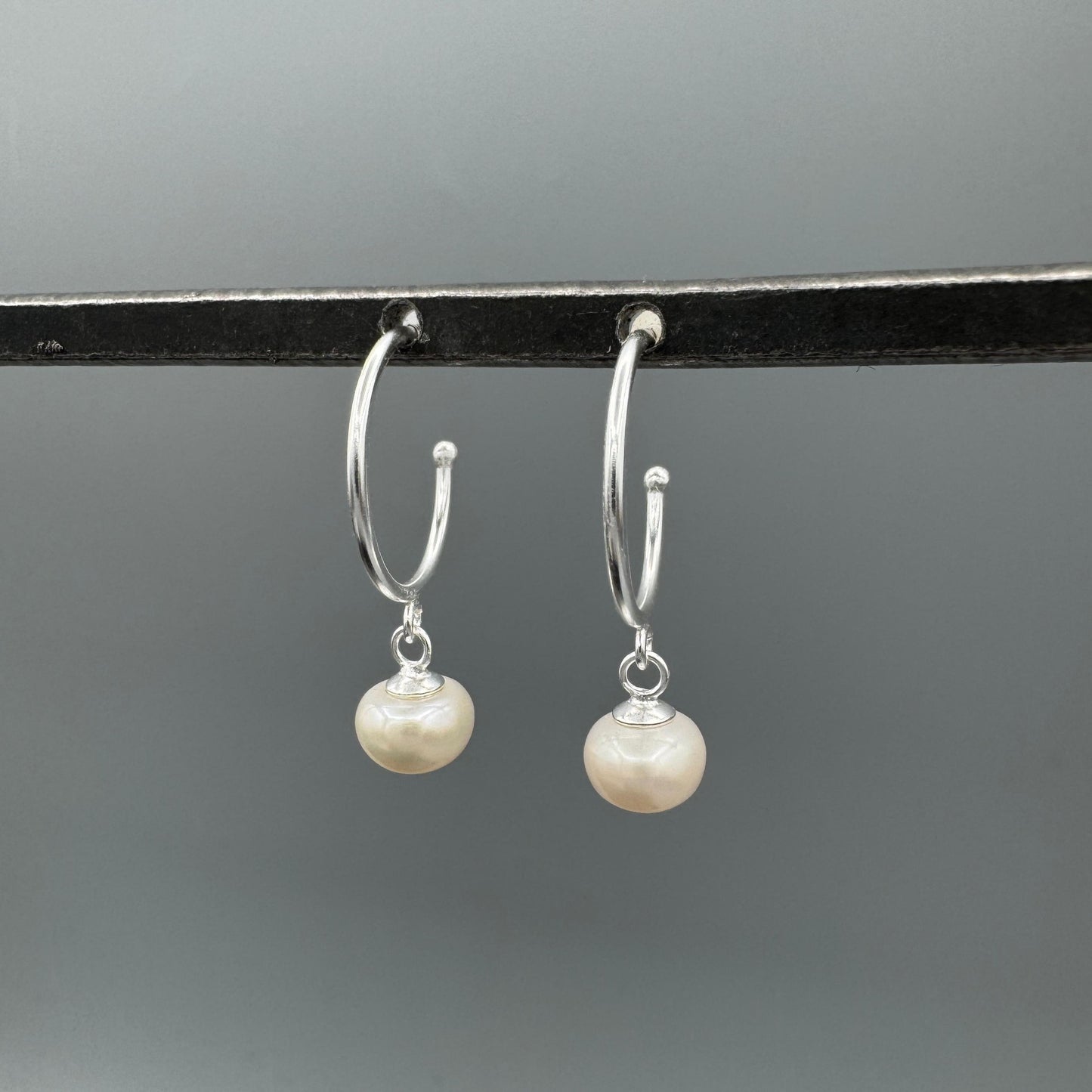 Silver hoop earrings with pearl drops on a gray background