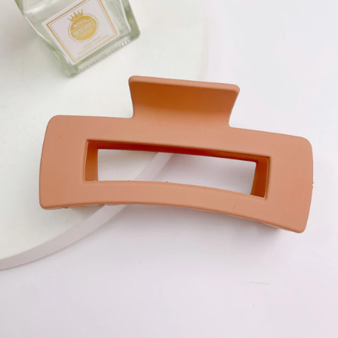 Desert Tan- colored hair clip on a white surface with a small green container in the background.