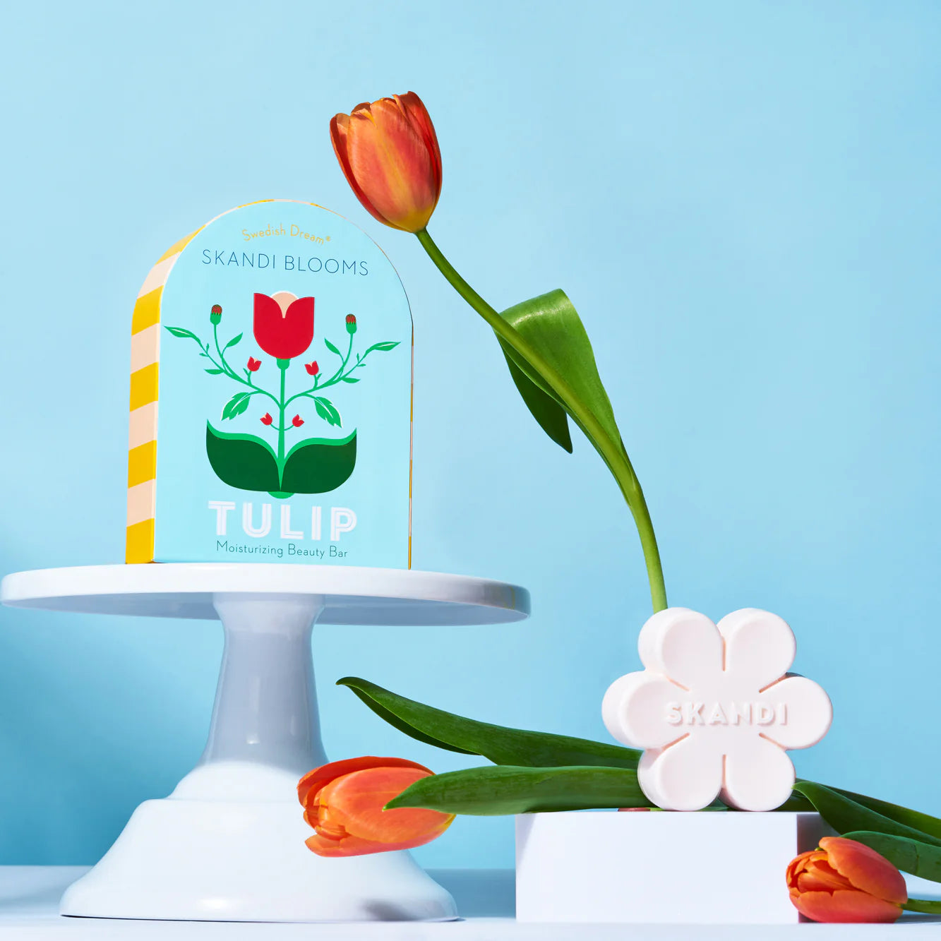 Skandi Bloom soap and it's box displayed on a cake stand wiht orange tulips