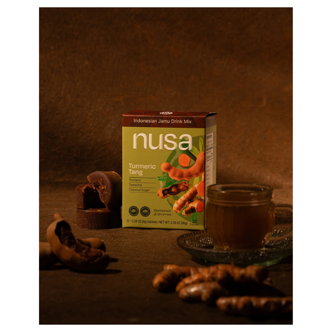 Nusa Turmeric Tang drink mix box with a cup and turmeric roots on a dark background.