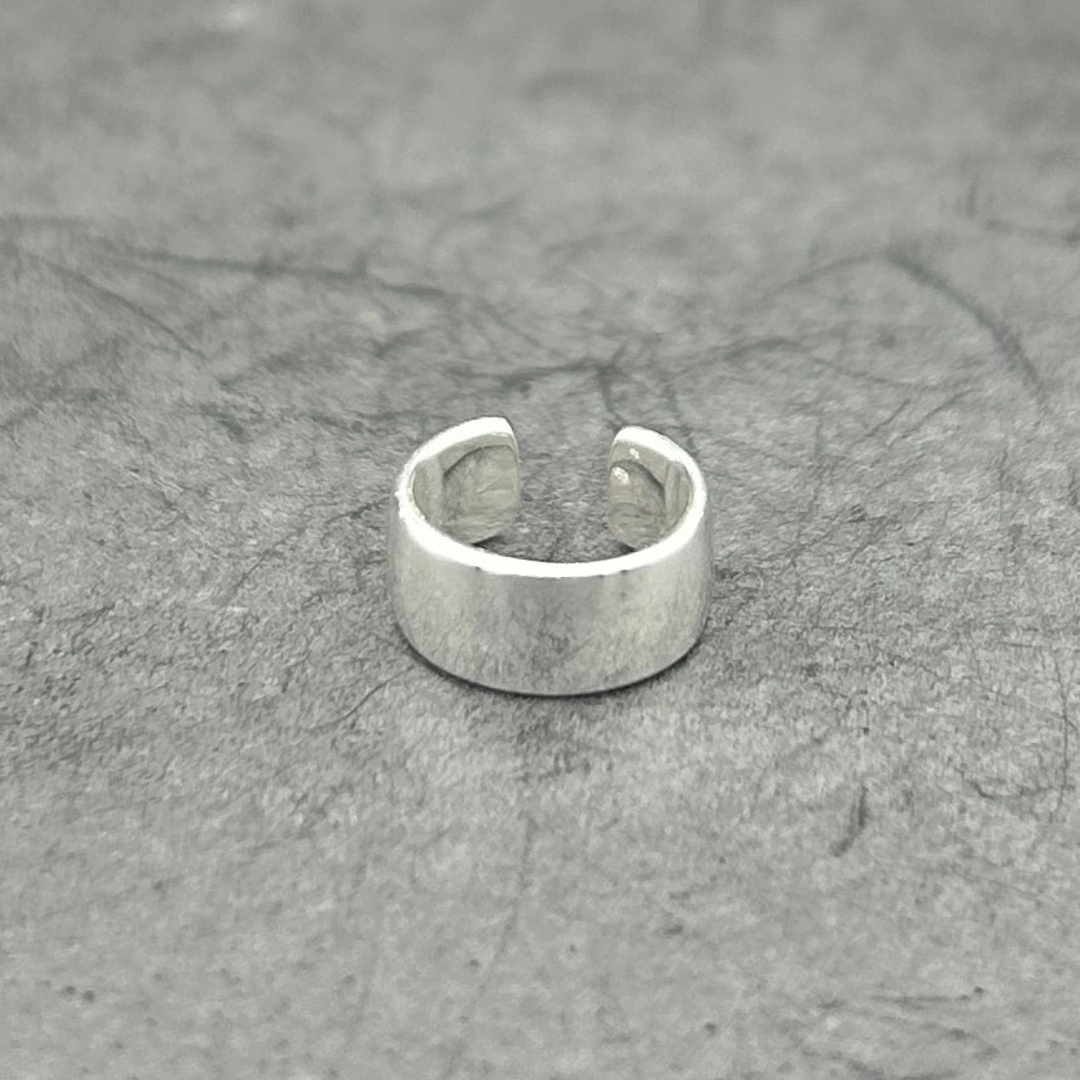 Wide silver ear cuff sitting atop of a gray surface.