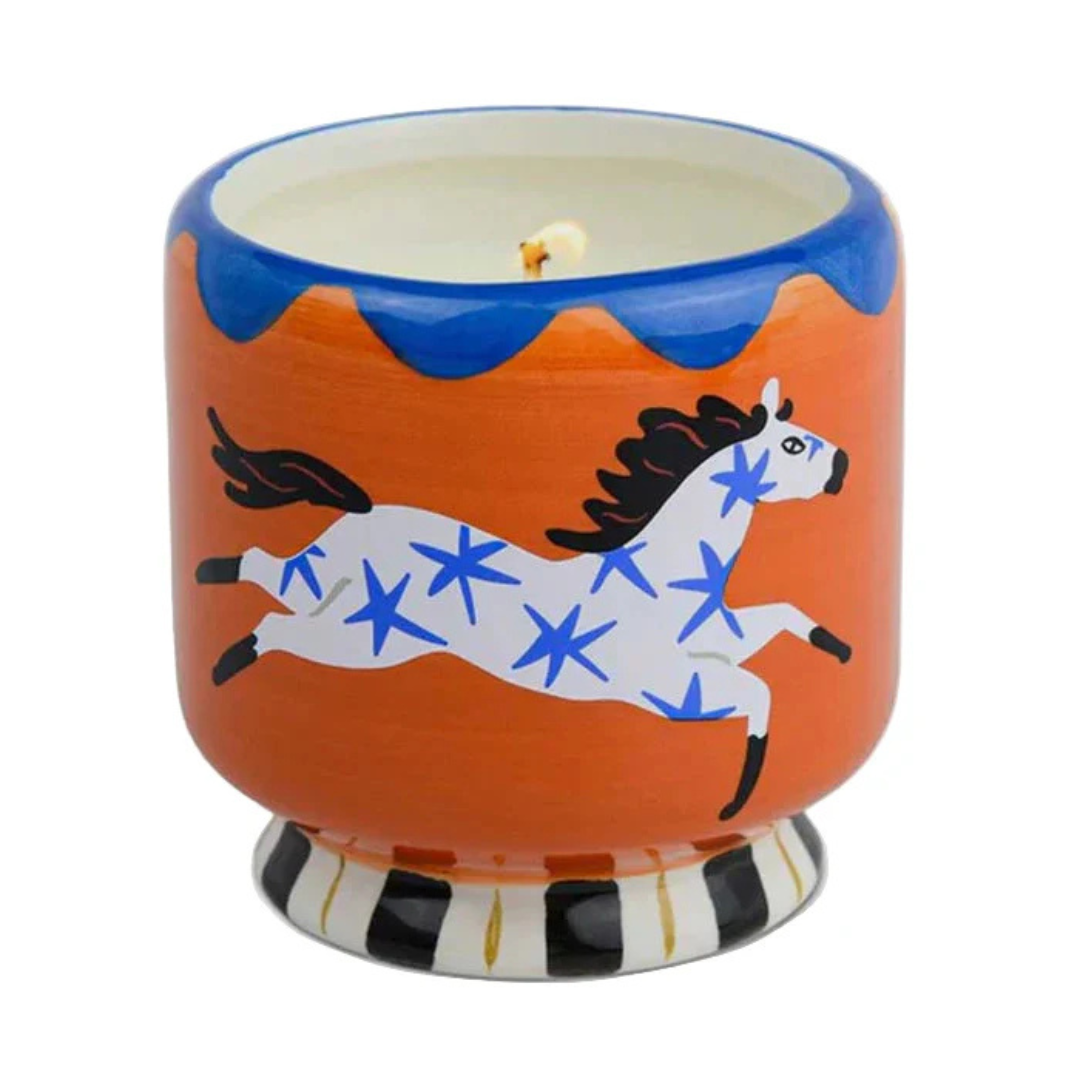 Candle in a decorative container with a horse design on an orange background