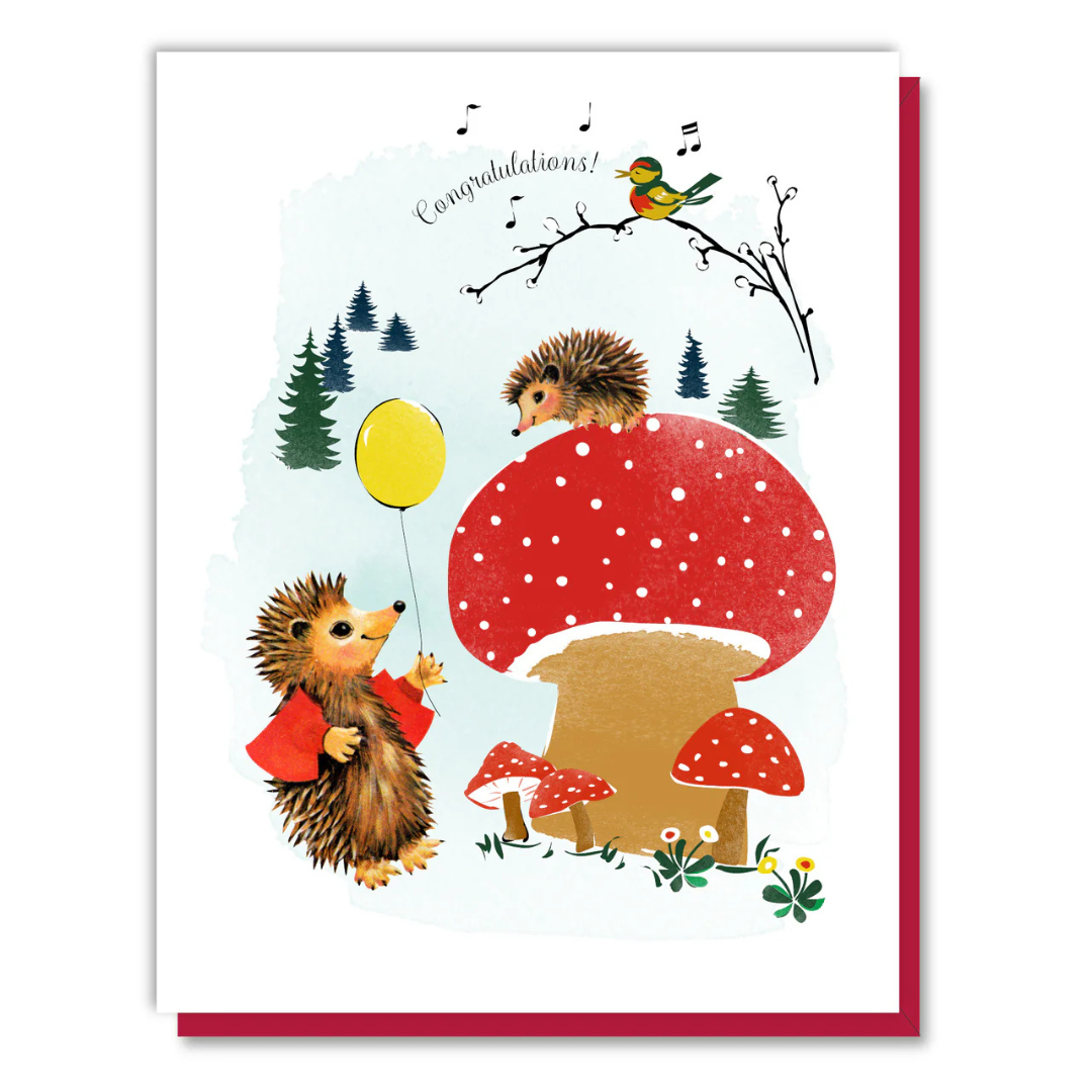 White congratulations card featuring brown hedgehogs and red mushrooms with one holding a yellow balloon.