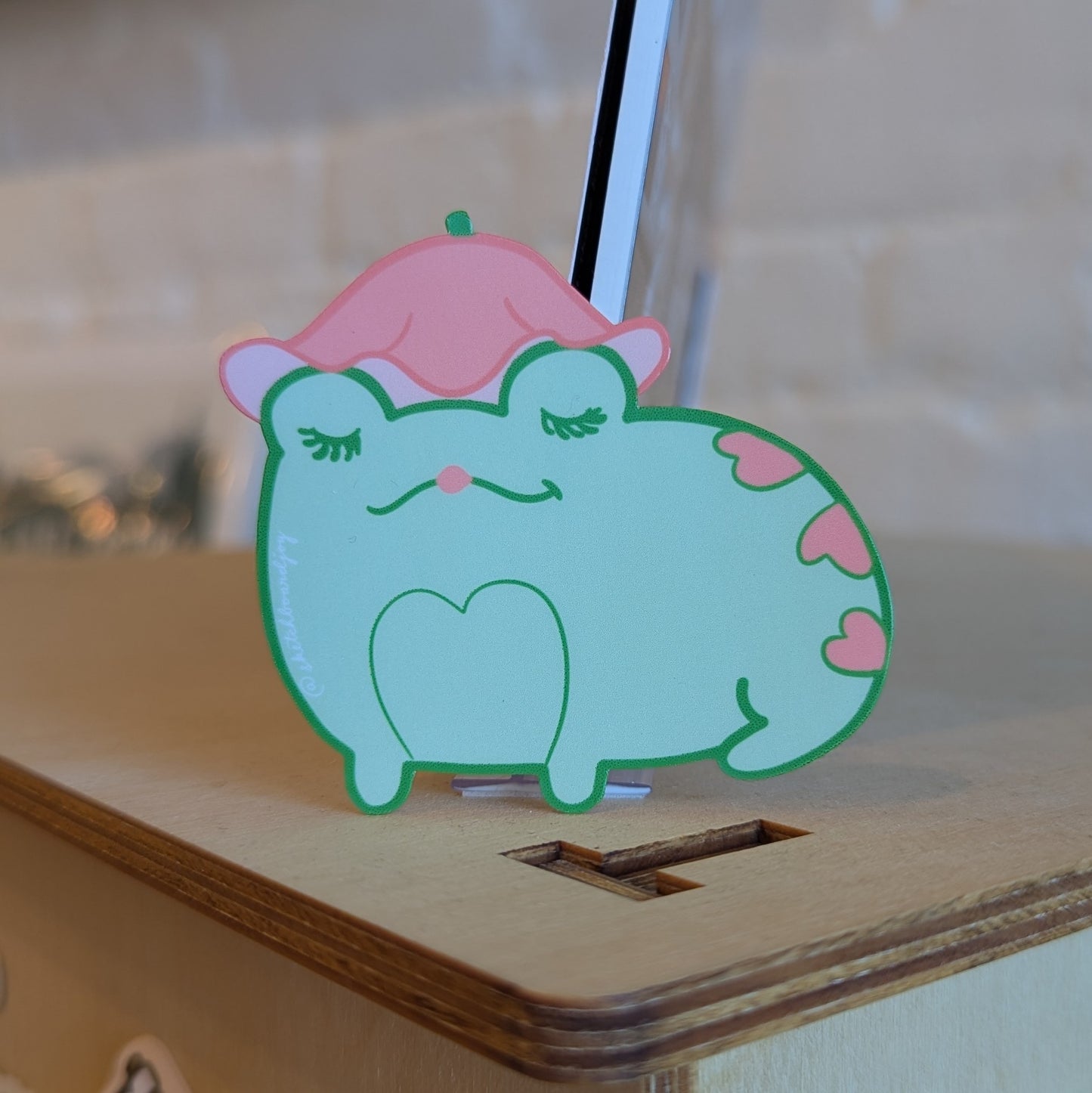 Sticker of a heart covered frog wearing a pink flower hat. It's very cute.