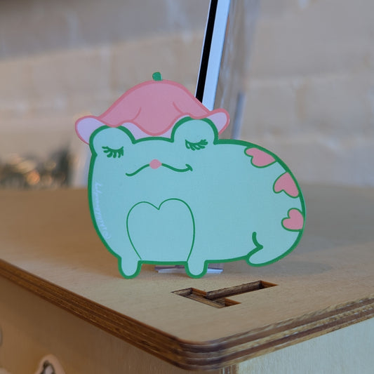Sticker of a heart covered frog wearing a pink flower hat. It's very cute.
