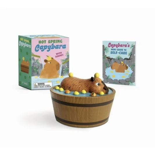 Mini plastic toy featuring a capybara in a hot spring tub. Illustrated box and book standing up behind toy.