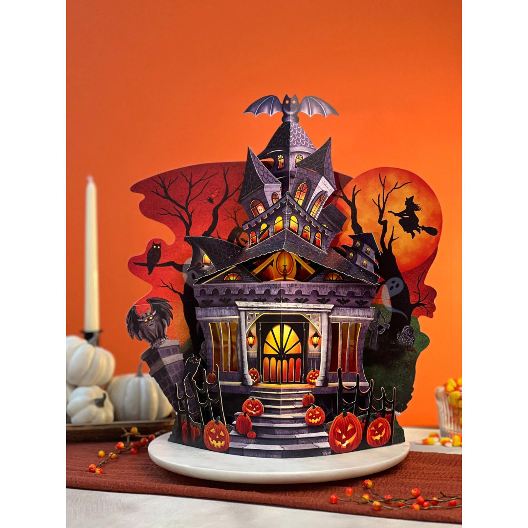 Haunted house pop-up card featuring black and purple haunted house with jack-o-lanterns, bats, a gargoyle, a witch, ghosts and an orange Halloween sky as a background.