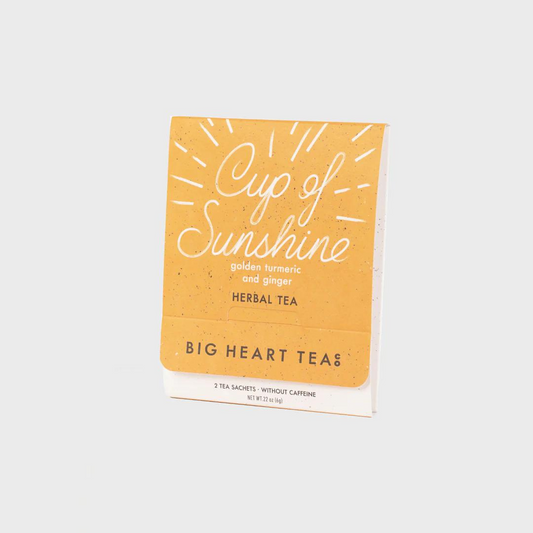 Yellow tea label featuring the title "Cup of Sunshine" in white cursive with a white sun ray design and the words "golden turmeric and ginger herbal tea" above the brand name "Big Heart Tea Co" in black lettering.