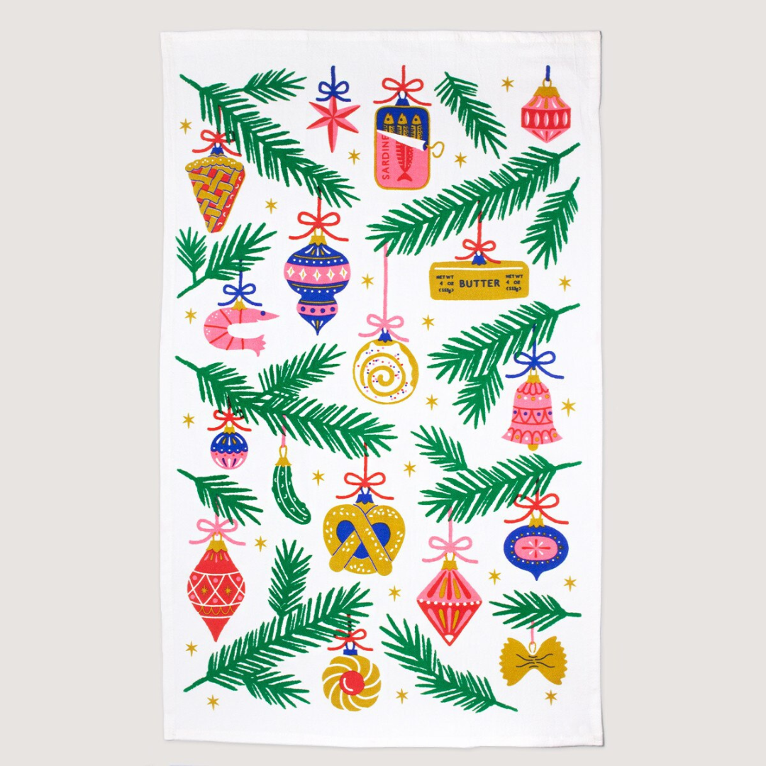 Kitchen towel with white background featuring green stems of Christmas trees and an assortment of blue, pink, red and gold Christmas ornaments.