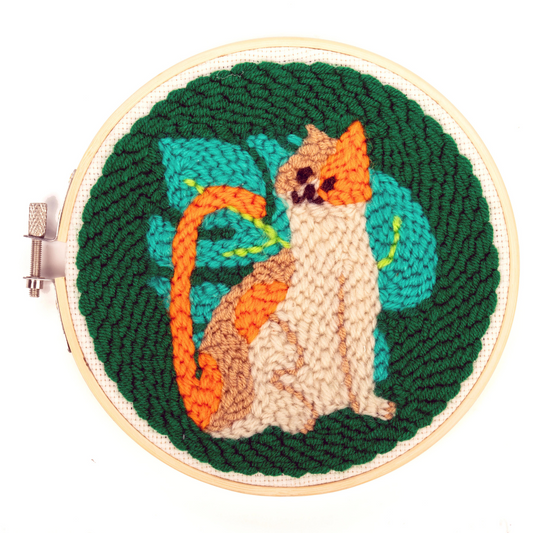 Finished punch needle kit of an orange and white cat with a green, leafy background.