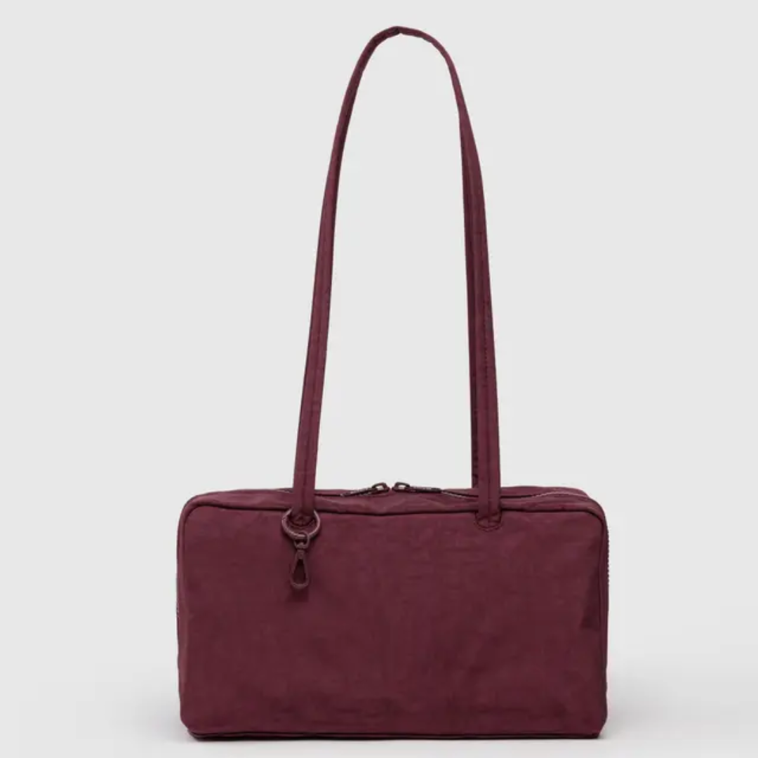 Baggu bowler bag is rectangular with a long shoulder strap. Bag is a brownish maroon.