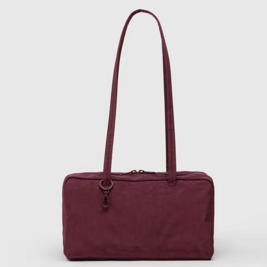 Baggu bowler bag is rectangular with a long shoulder strap. Bag is a brownish maroon.