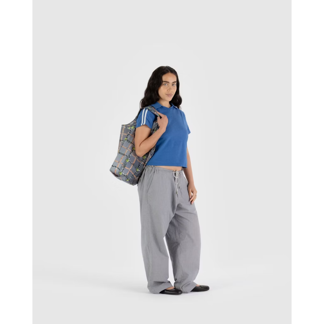 Woman holding a gray reusable tote bag featuring a pattern of beaded chains appearing in a plaid pattern.