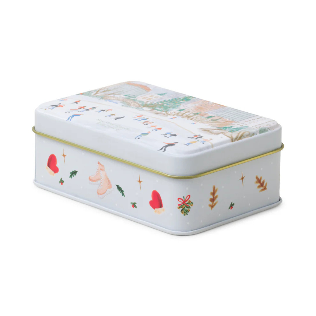 White holiday tin box featuring design of pink ice skates, red mittens and brown leaves. Gold piping on the sides.