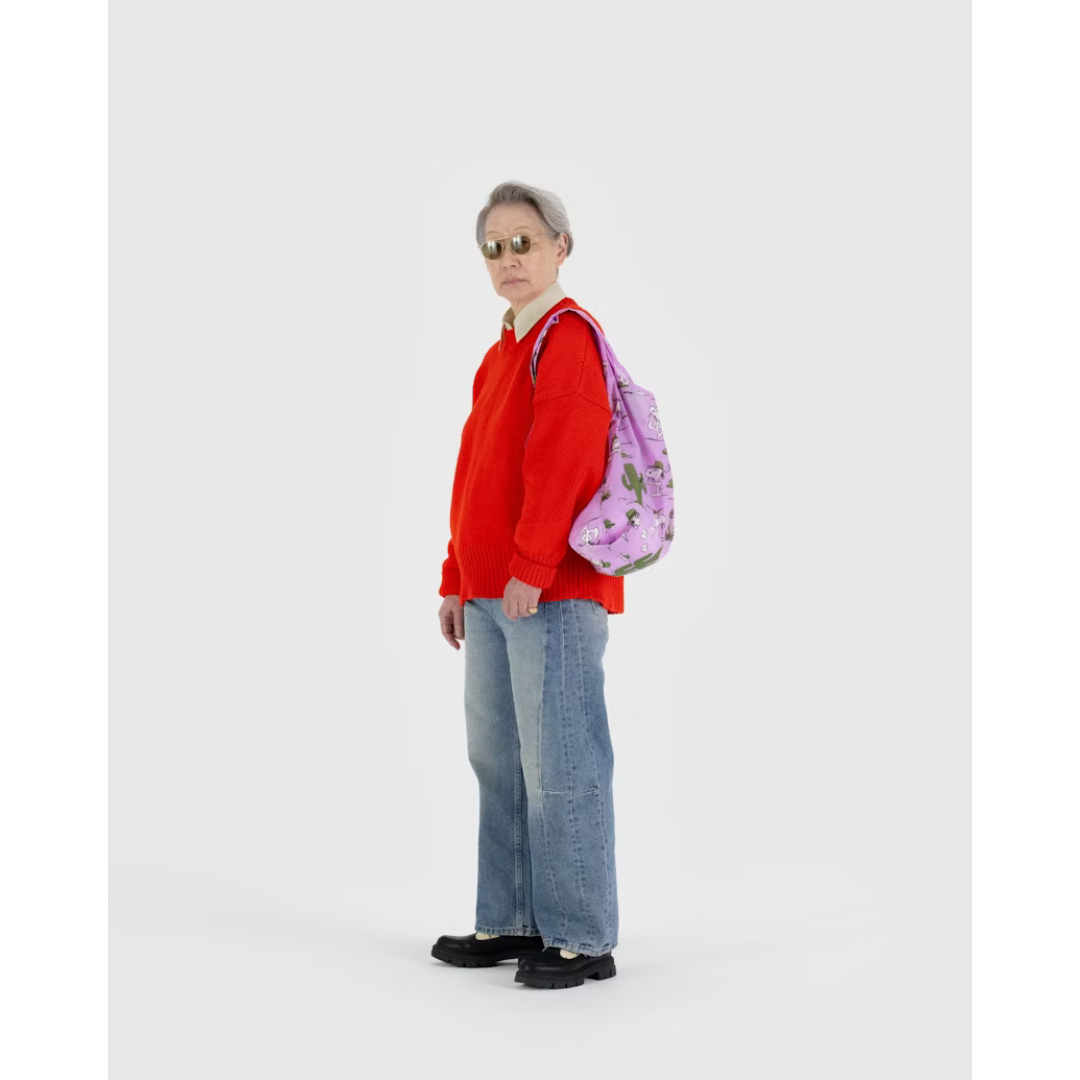 Woman in red carrying pink reusable tote bag featuring a pattern with a white dog wearing a green hat holding a magnifying glass and green cacti.