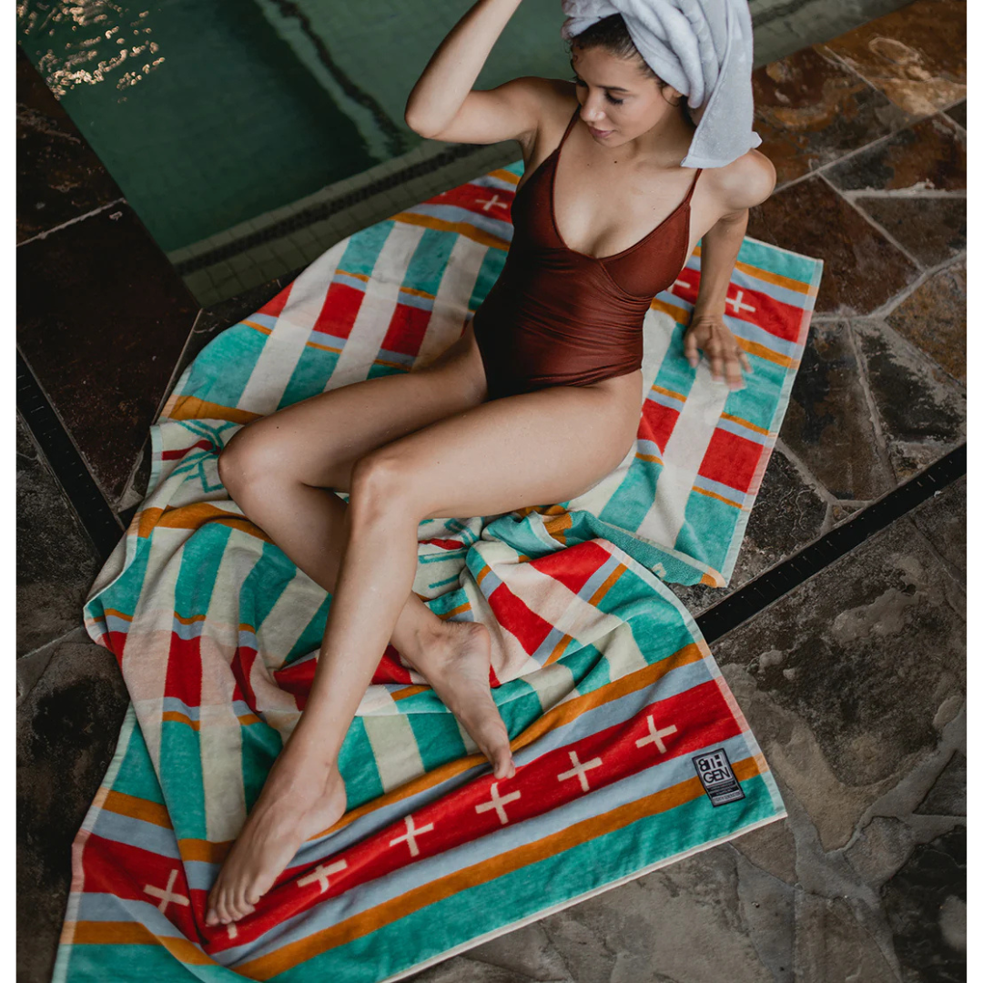 Woman in swimsuit laying across striped beach towel.