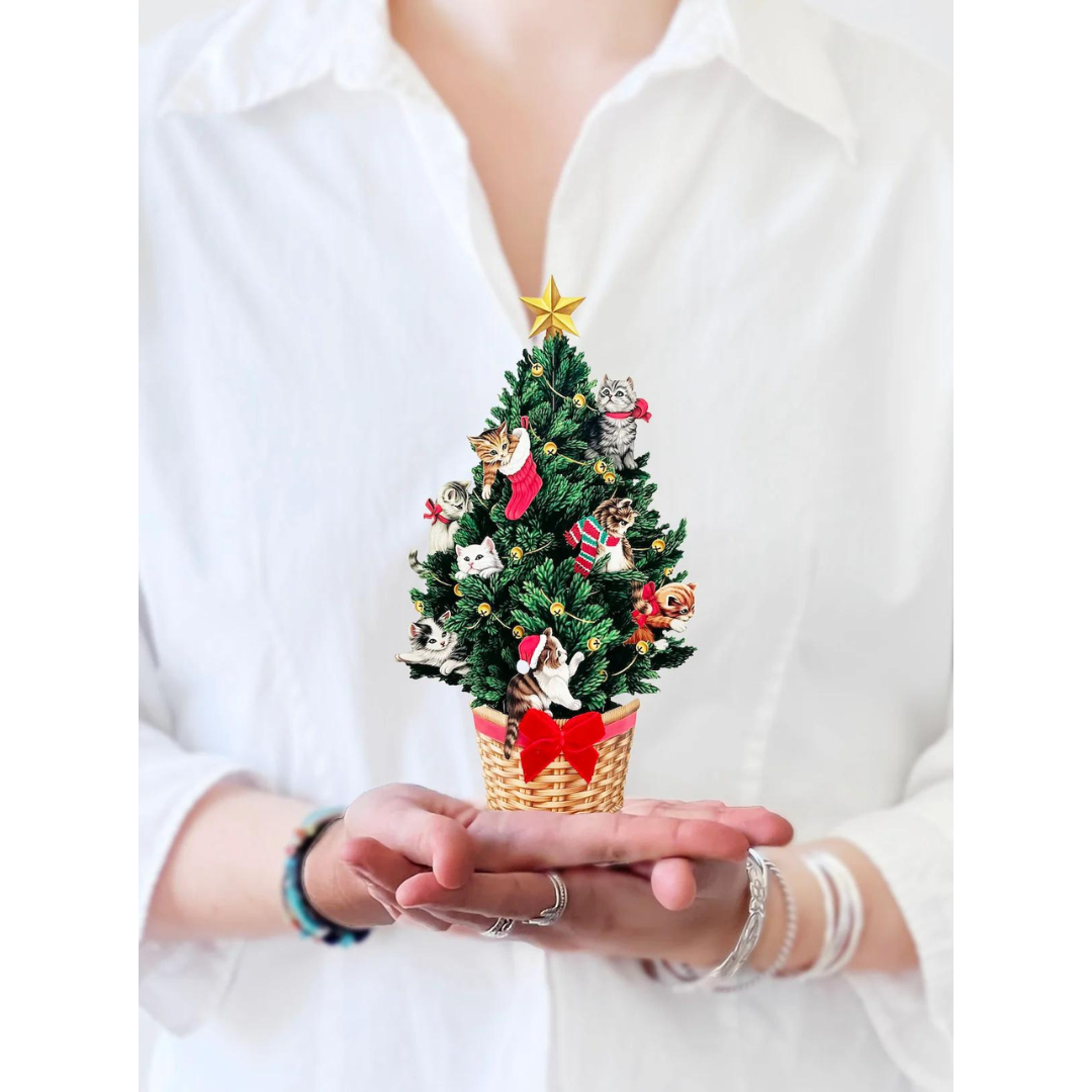 Woman in white holding mini Christmas tree pop-up card featuring kitten ornaments, all in the palm of her hands.