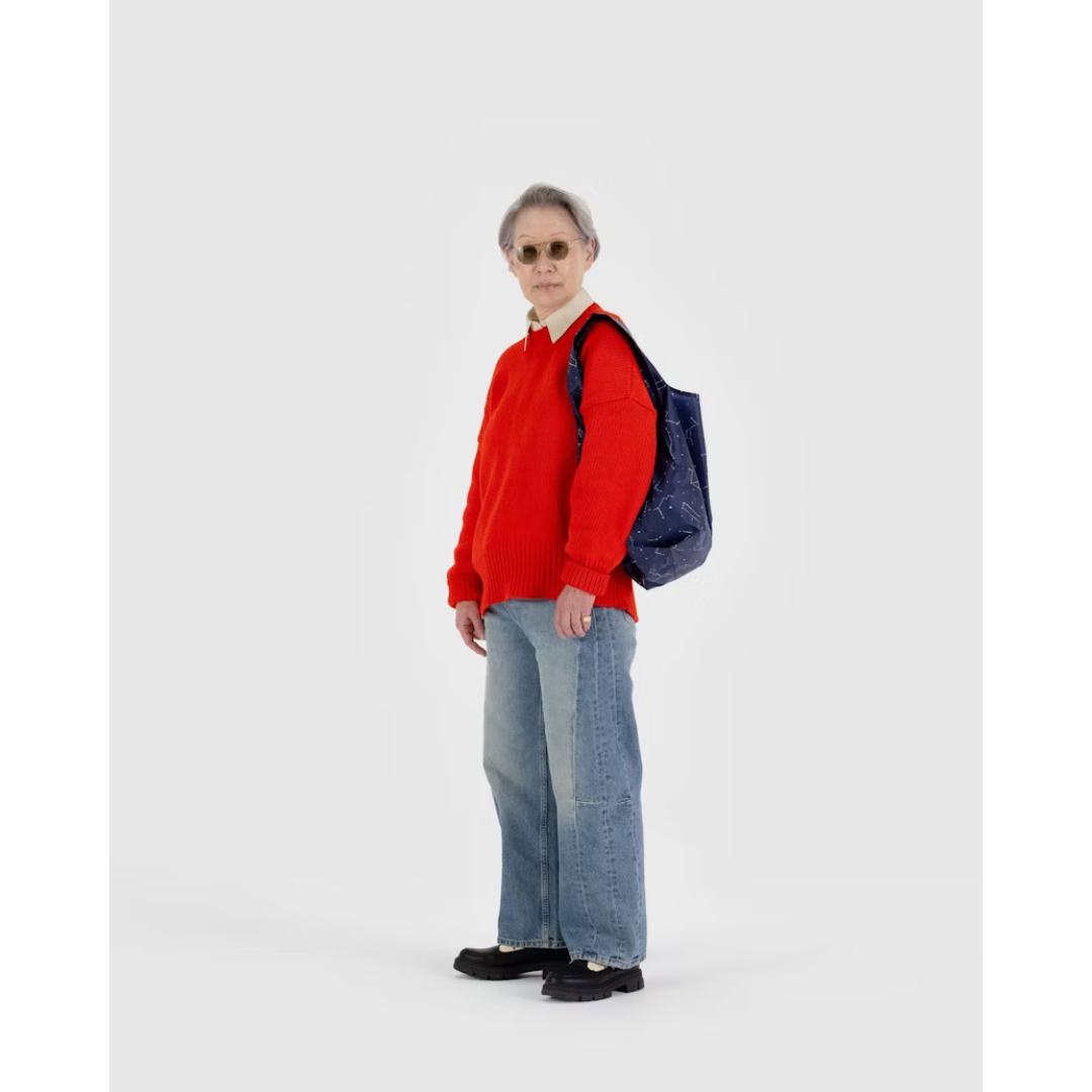 Woman carrying a navy blue reusable tote bag featuring an all over constellation print.