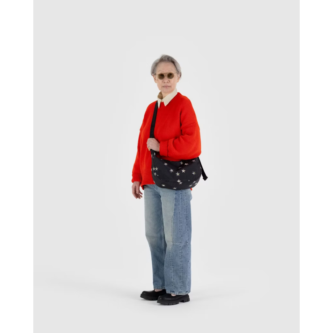 Woman carrying a black nylon bag in a crescent shape featuring an all over silver starts pattern and a black strap.