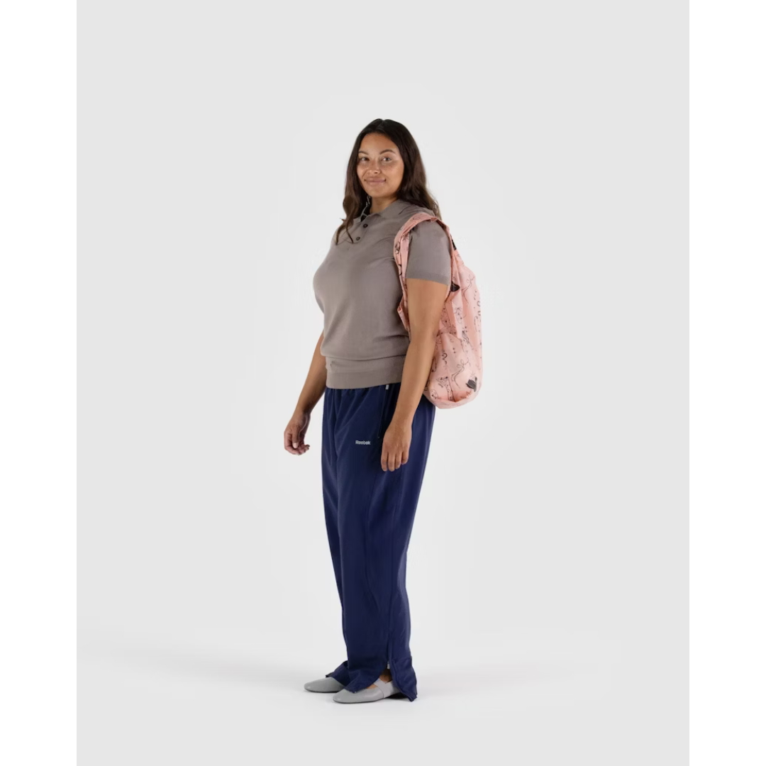 Woman carrying baby pink reusable tote bag featuring a  black pattern of swans, moons and stars, bows and ballet slippers.