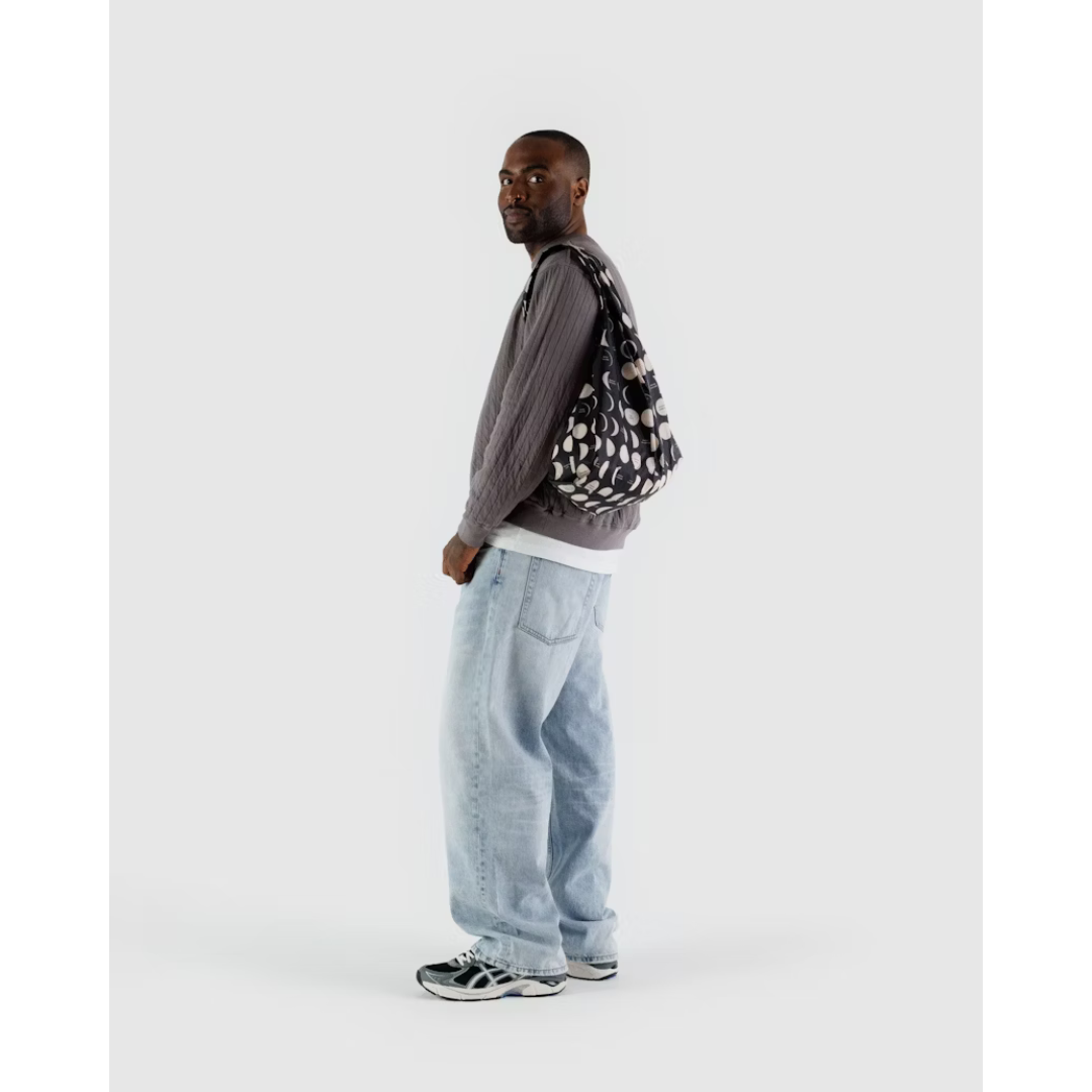 Man holding black reusable tote bag featuring different phases of the moon in white.