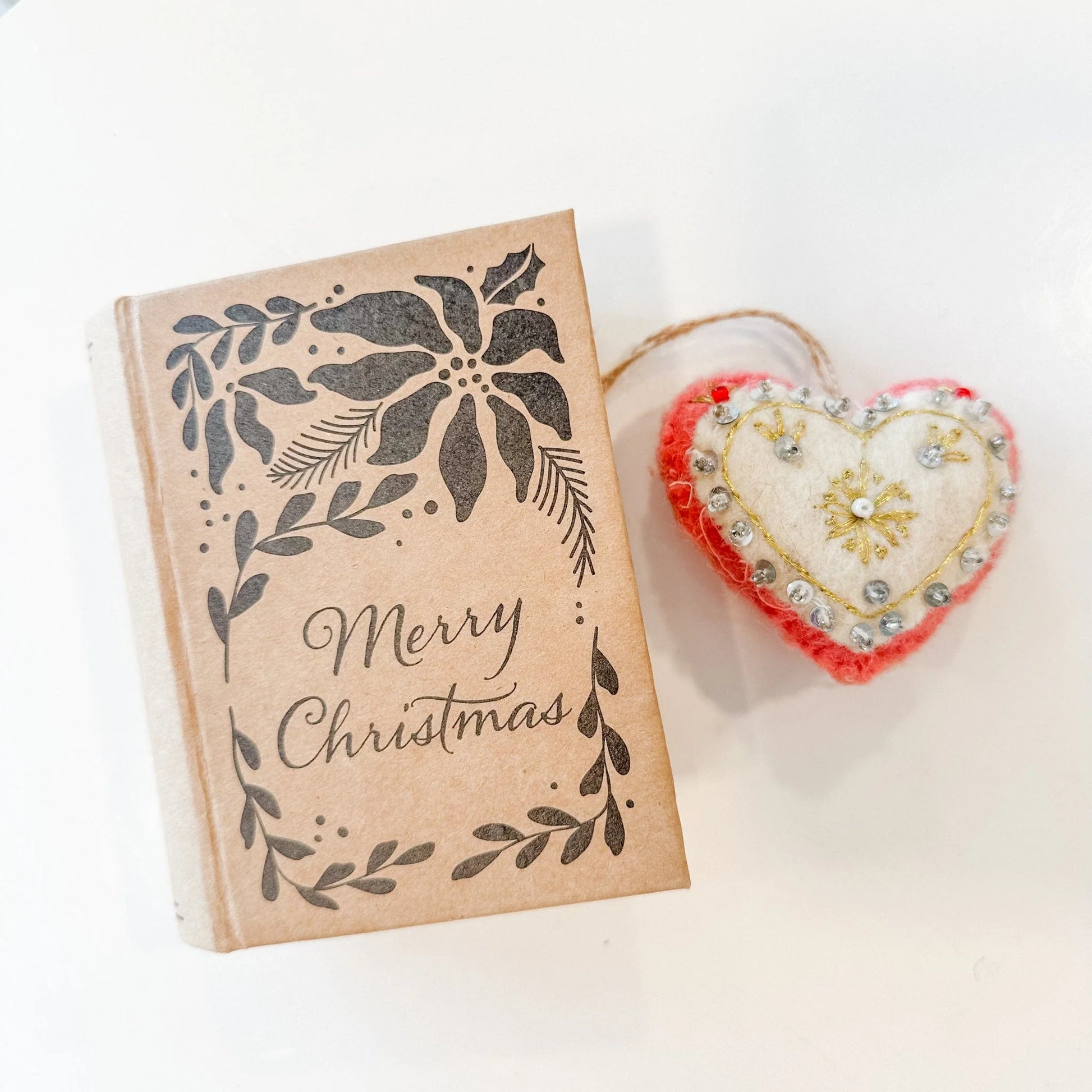 Red and white heart decorated with gold embroidery and silver beads and sequins with a book-shaped box that reads "Merry Christmas"
