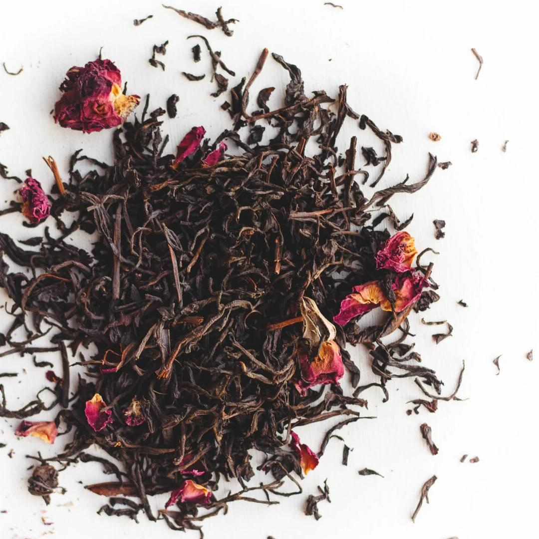 Loose Ear Grey black tea leaves with an accent of dried rose petals against a white background.