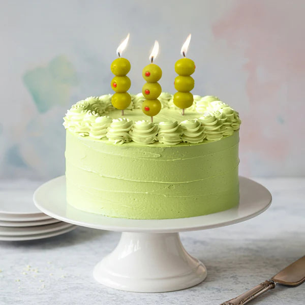 Green frosted cake  on a white cake-stand with 3 of the olive candles aglow on top.