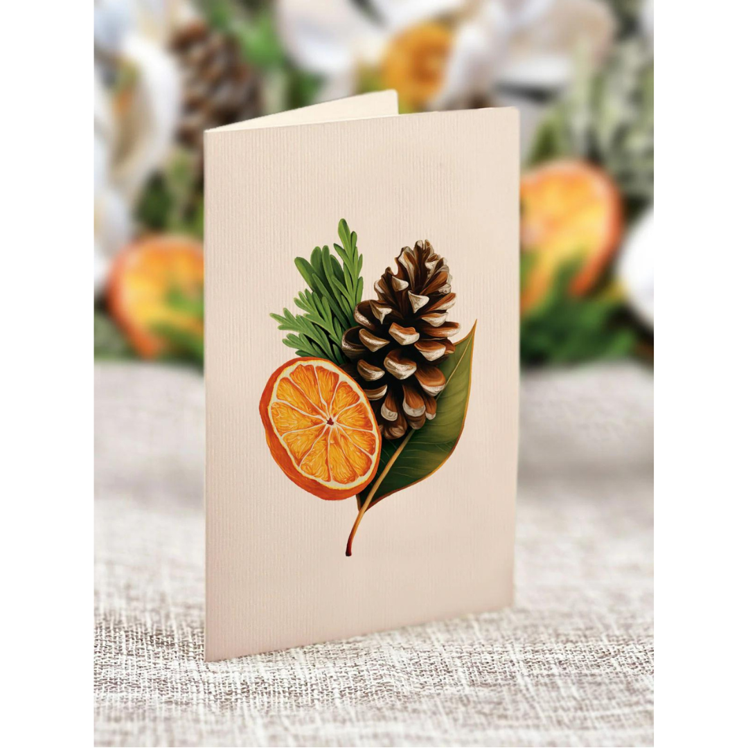 Blank white greeting card featuring graphic of a pinecone, orange slice and pieces of greenery.