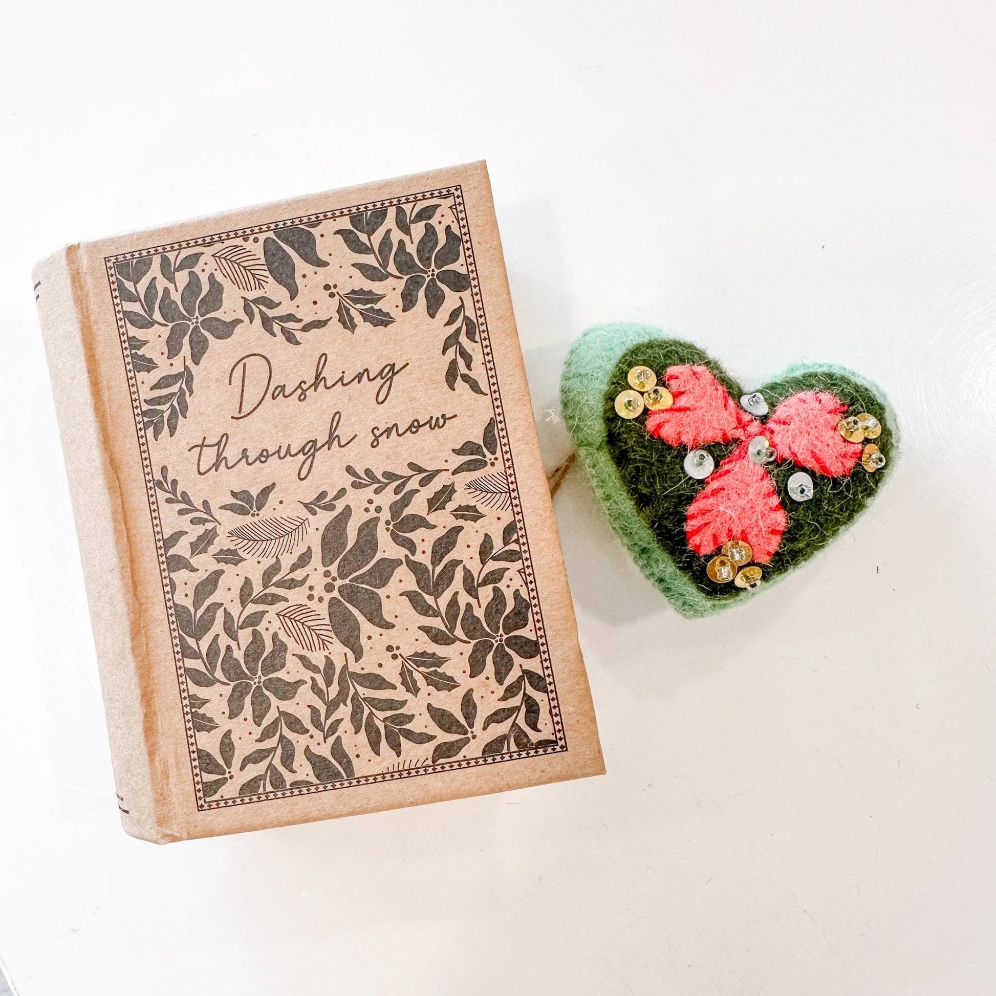 Green and pink heart shaped ornament decorated with pink hearts and gold & sliver sequins with a book-shaped box that says "Dashing through snow"