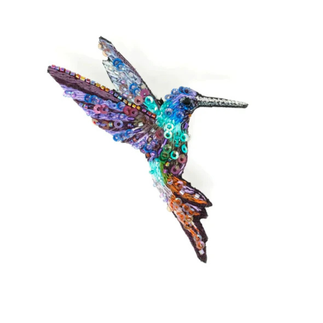 Hand embroidered and beaded hummingbird brooch. The little guy is a riot of color with a blue, purple, and silver on it's wings, a blue and purple head with a silver beak, a green body and orange and purple in it's tail. Brooch is covered in blue, purple, green, and clear iridescent micro sequins and beads.
It's very sparkly. 