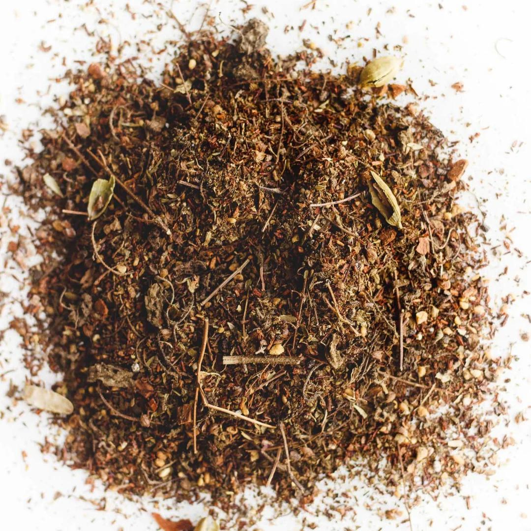 Loose Chai tea leaves featuring ground cinnamon, allspice, ginger and star anise against a white background.