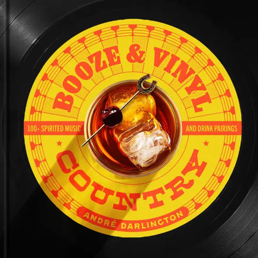 Cover for "Booze & Vinyl Country: 100+ Spirited Music and Drink Parings" looks like the vinyl record with a yellow and red label. At the center of the record rests an old fashioned with a dark cherry on a toothpick with a horseshoe decoration.