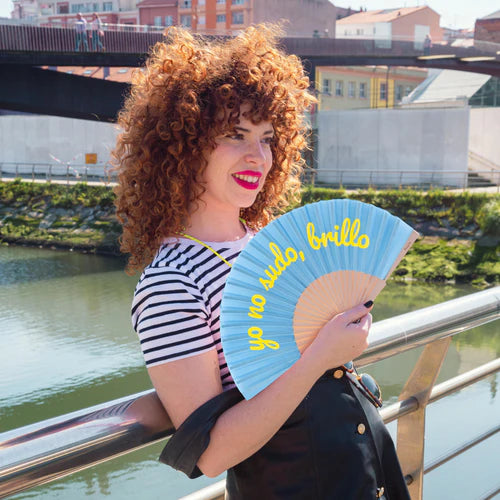 Model with curly red hair holds a fan by a river