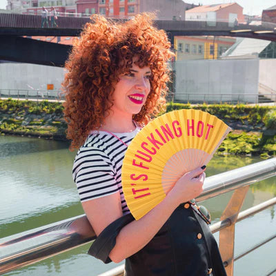 Model with red hair in a striped shirt holds fan near a river