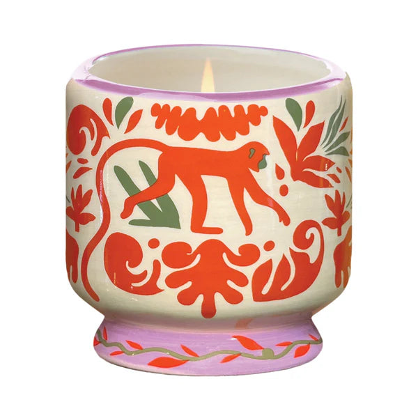 Candle with a ceramic container with a painted orange jungle motif featuring a monkey.