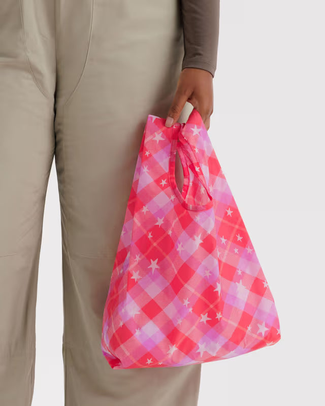 Person holding a pink and purple checkered bag against a neutral background