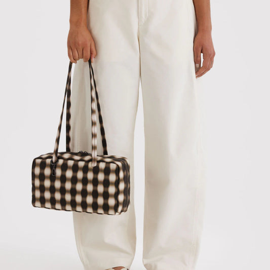 Person holding a checkered bag with white pants on a plain background
